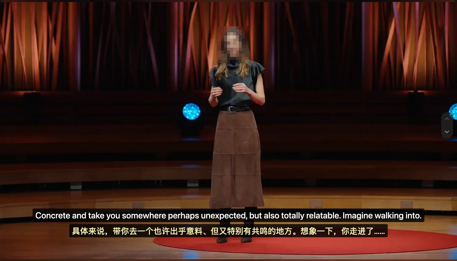 Sprecher auf einer mit rotem Teppich ausgelegten Bühne mit zwei Zeilen Equalang-Untertiteln am unteren Rand: englisches Original mit dem Text 'Concrete and take you somewhere perhaps unexpected, but also totally relatable. Imagine walking into.' und chinesische Übersetzung mit dem Text '具体来说，带你去一个也许出乎意料、但又特别有共鸣的地方。想象一下，你走进了……'